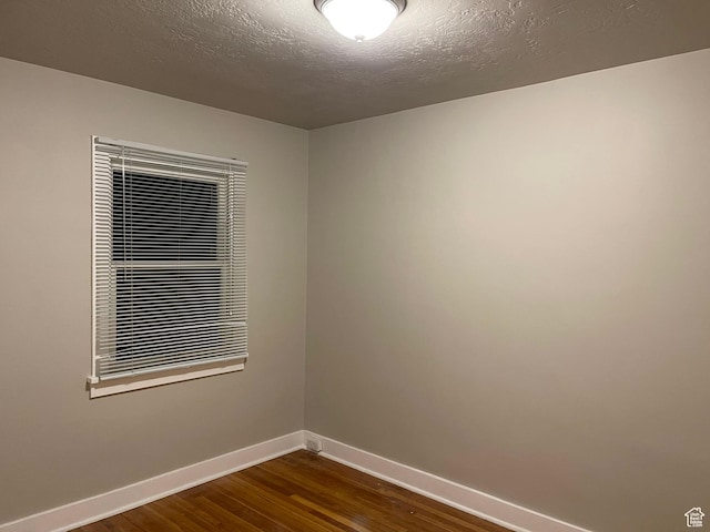unfurnished room with dark wood-style floors, a textured ceiling, and baseboards