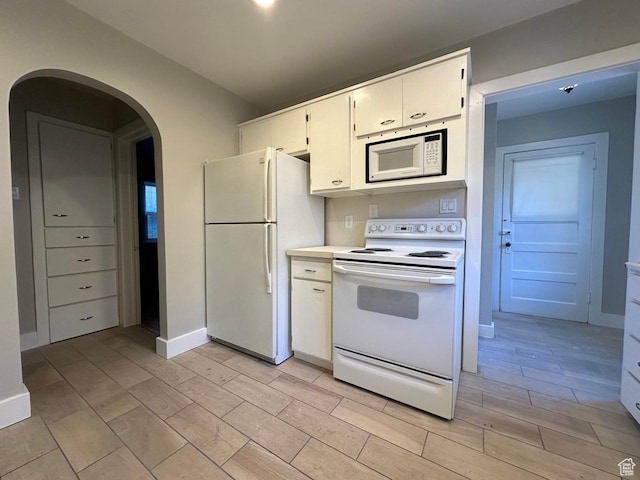 kitchen featuring wood finish floors, white appliances, arched walkways, white cabinets, and light countertops