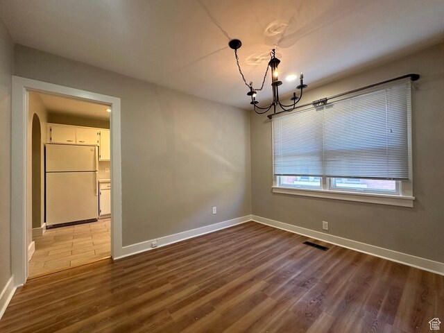 spare room with a chandelier, arched walkways, baseboards, and wood finished floors