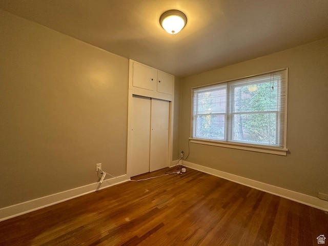unfurnished bedroom with dark wood finished floors, a closet, and baseboards