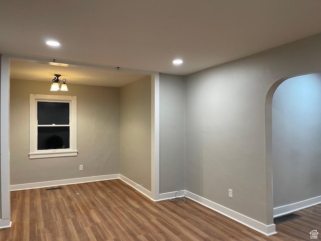 unfurnished room with arched walkways, wood finished floors, visible vents, and baseboards