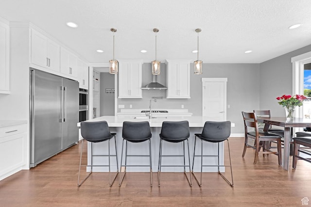 kitchen with light countertops, wall chimney range hood, white cabinets, and appliances with stainless steel finishes