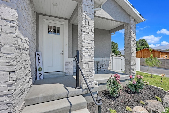 property entrance featuring stone siding, covered porch, and fence