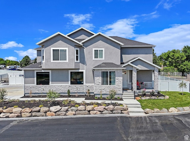 view of front facade with fence, a shingled roof, stucco siding, a front lawn, and stone siding