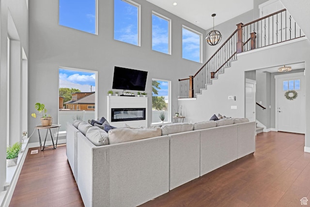 living room featuring stairs, an inviting chandelier, dark wood-style flooring, and a glass covered fireplace