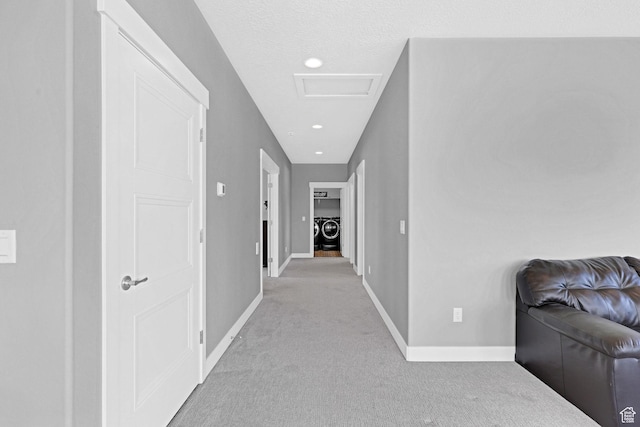 hallway featuring baseboards, attic access, washer / clothes dryer, a textured ceiling, and light colored carpet