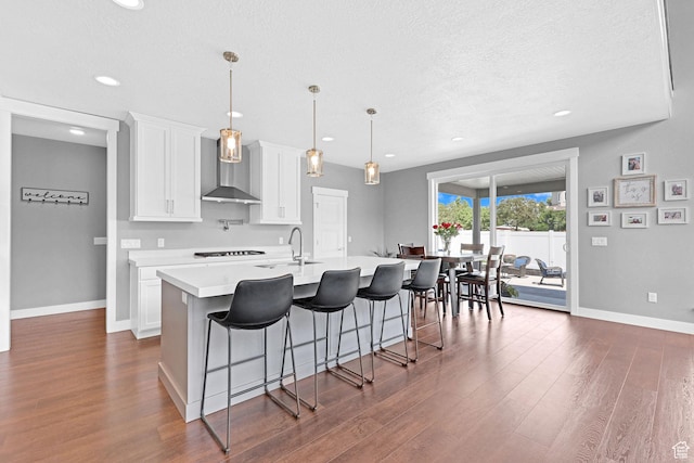 kitchen featuring a center island with sink, a breakfast bar, light countertops, white cabinetry, and wall chimney exhaust hood