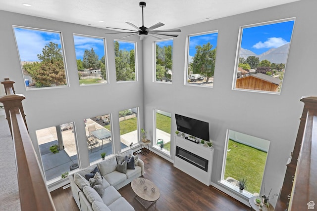 living area featuring a wealth of natural light, wood finished floors, a glass covered fireplace, and a ceiling fan