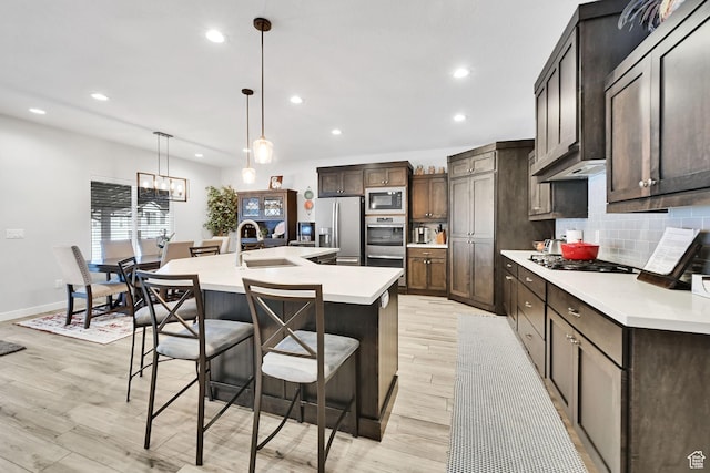 kitchen with a center island with sink, a sink, appliances with stainless steel finishes, light countertops, and decorative backsplash