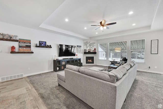 living area featuring a tray ceiling, visible vents, baseboards, and a tiled fireplace