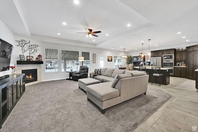 living room with a tiled fireplace, a raised ceiling, and recessed lighting