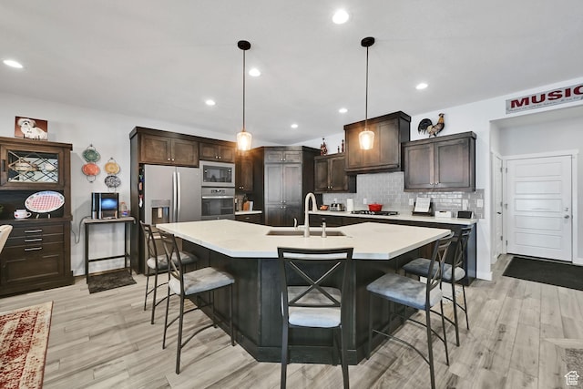 kitchen with a breakfast bar area, light countertops, decorative backsplash, appliances with stainless steel finishes, and a sink