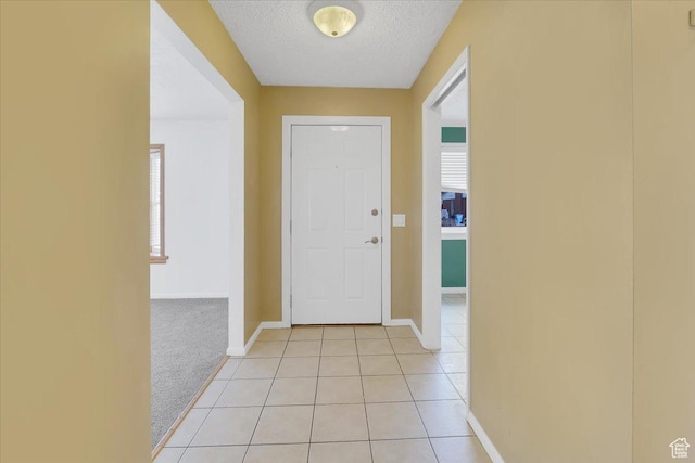 entryway featuring light carpet, light tile patterned floors, baseboards, and a textured ceiling
