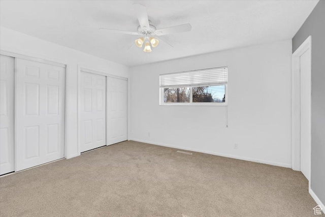 unfurnished bedroom featuring baseboards, carpet floors, a ceiling fan, and multiple closets