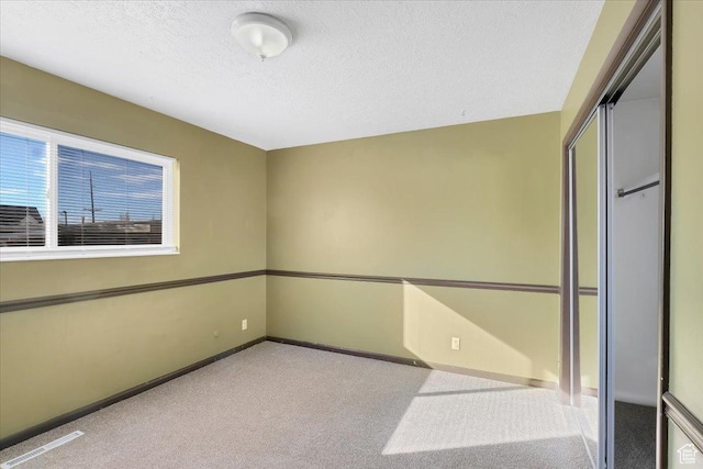 empty room featuring carpet flooring, a textured ceiling, and baseboards