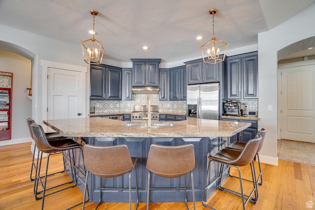 kitchen with stainless steel fridge with ice dispenser, arched walkways, a chandelier, under cabinet range hood, and light wood-style flooring