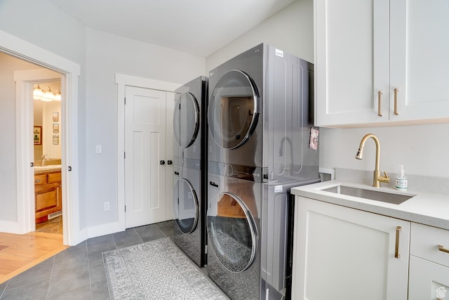 clothes washing area featuring tile patterned flooring, stacked washer / dryer, a sink, baseboards, and cabinet space