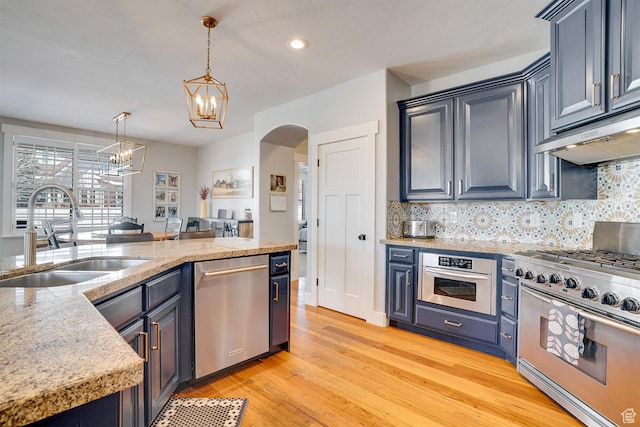 kitchen with a notable chandelier, under cabinet range hood, appliances with stainless steel finishes, arched walkways, and a sink