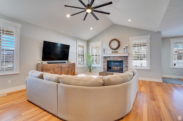 living room featuring baseboards, light wood-type flooring, a stone fireplace, vaulted ceiling, and ceiling fan