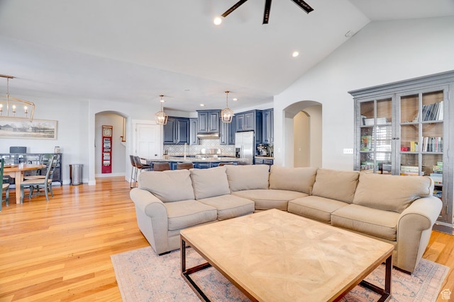living area with ceiling fan with notable chandelier, high vaulted ceiling, arched walkways, recessed lighting, and light wood finished floors