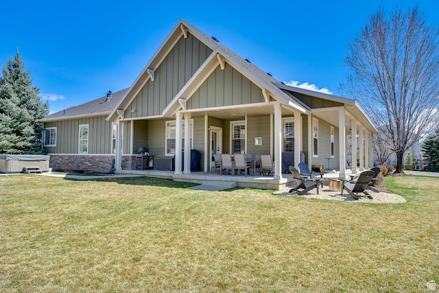 back of house featuring a patio, a fire pit, board and batten siding, a hot tub, and a lawn