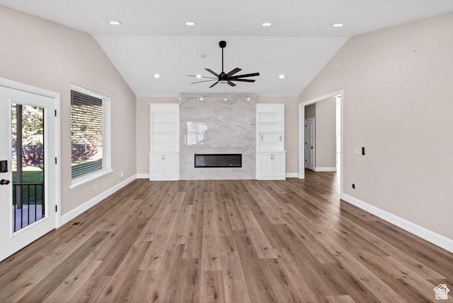 unfurnished living room featuring lofted ceiling, built in shelves, wood finished floors, baseboards, and a fireplace