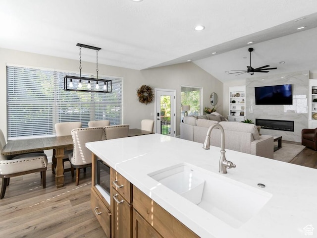 kitchen featuring brown cabinetry, a sink, light wood-style flooring, lofted ceiling, and built in microwave