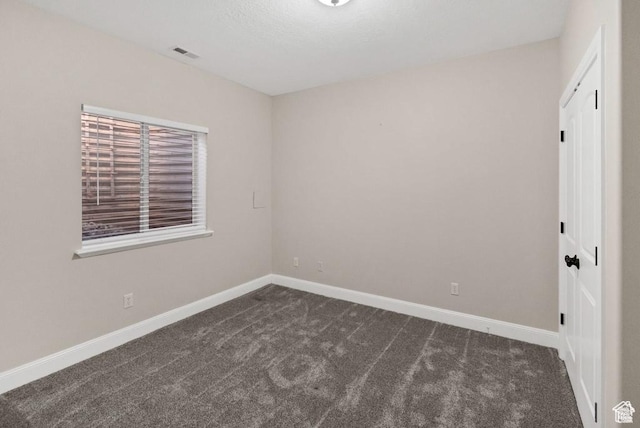 unfurnished room featuring dark carpet and baseboards
