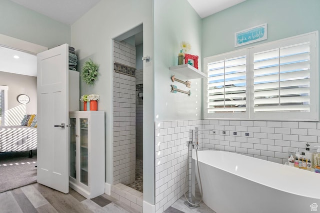 bathroom with walk in shower, a freestanding tub, wood finished floors, wainscoting, and tile walls