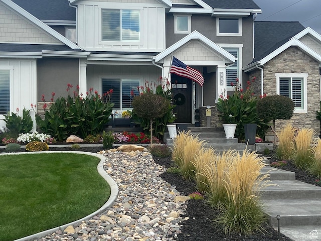 exterior space featuring a shingled roof, stone siding, a front lawn, and board and batten siding