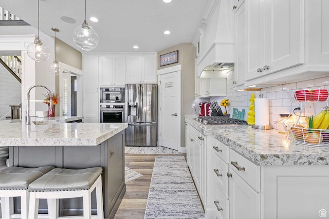 kitchen with a kitchen breakfast bar, white cabinets, a sink, stainless steel appliances, and custom range hood