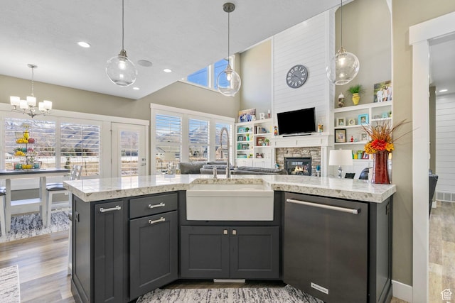 kitchen featuring a stone fireplace, a chandelier, dishwasher, a sink, and open floor plan