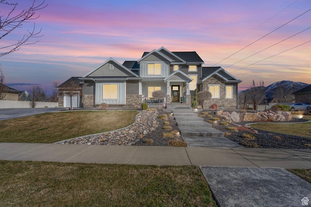 craftsman-style house with concrete driveway, stone siding, and a lawn