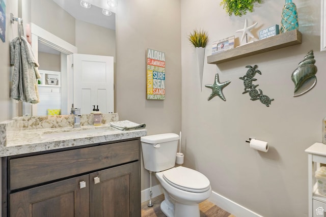 half bath with toilet, wood finished floors, vanity, and baseboards