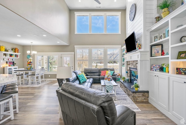 living room featuring an inviting chandelier, a stone fireplace, recessed lighting, a towering ceiling, and light wood-style flooring