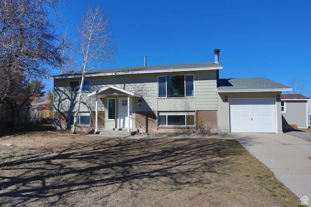 bi-level home with brick siding, an attached garage, concrete driveway, and fence