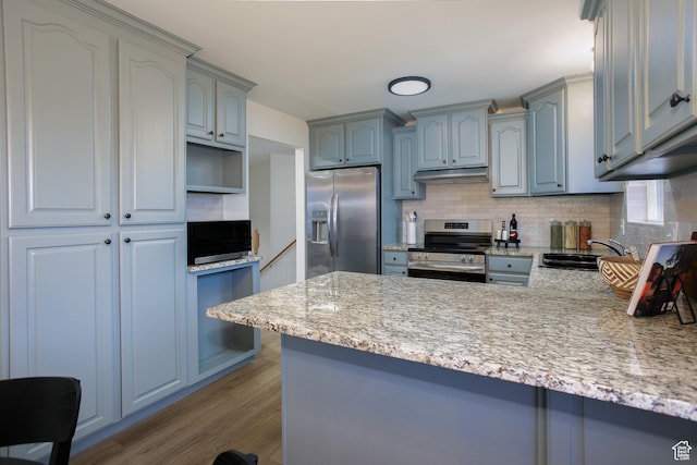 kitchen with under cabinet range hood, tasteful backsplash, wood finished floors, stainless steel appliances, and a peninsula