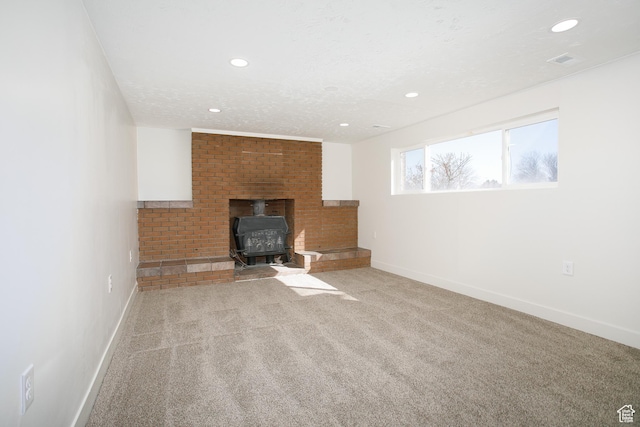unfurnished living room with visible vents, a textured ceiling, a wood stove, and carpet