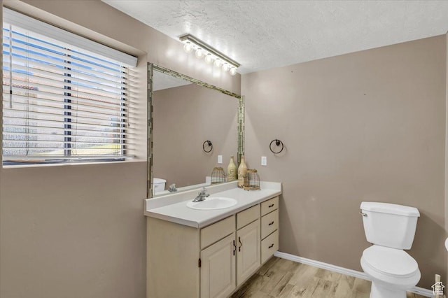 bathroom featuring baseboards, toilet, vanity, wood finished floors, and a textured ceiling