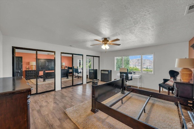 bedroom featuring visible vents, multiple closets, a textured ceiling, and wood finished floors