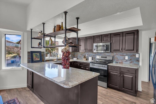kitchen featuring light wood-style flooring, tasteful backsplash, appliances with stainless steel finishes, and a peninsula