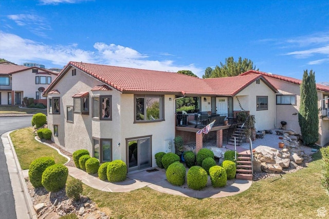 view of front of home with stairs, a tile roof, a front lawn, and stucco siding
