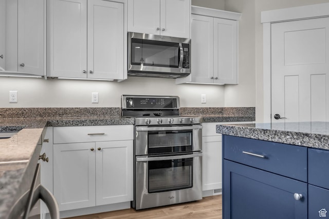 203 E Deer Run Loop Unit 40, Elk Ridge, UT 84651 - kitchen with stainless steel appliances, white cabinetry, light wood-style floors, blue cabinets, and dark stone countertops