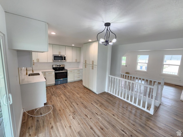 kitchen featuring light wood finished floors, a sink, stainless steel appliances, light countertops, and a notable chandelier