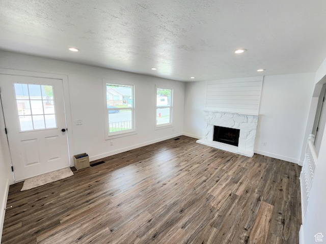 unfurnished living room featuring baseboards, visible vents, dark wood finished floors, a fireplace, and a textured ceiling