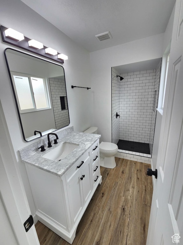 bathroom with vanity, wood finished floors, visible vents, a tile shower, and toilet
