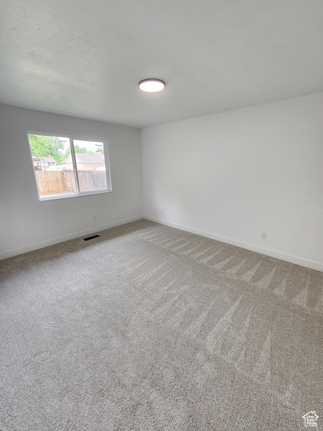 carpeted spare room featuring visible vents, baseboards, and a textured ceiling
