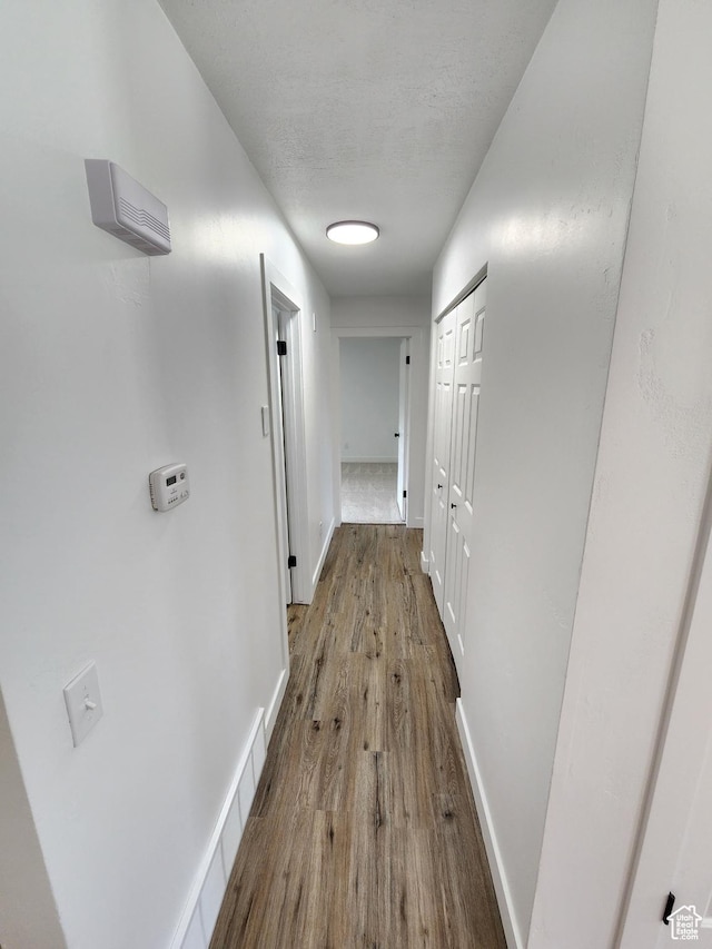 hallway with visible vents, wood finished floors, baseboards, and a textured ceiling