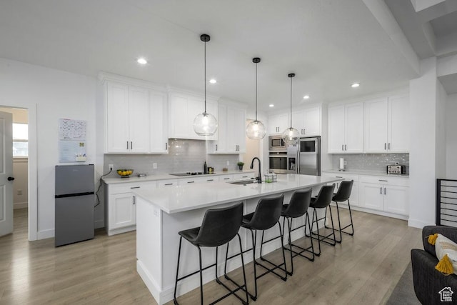 kitchen featuring a center island with sink, a sink, light wood-style floors, appliances with stainless steel finishes, and light countertops