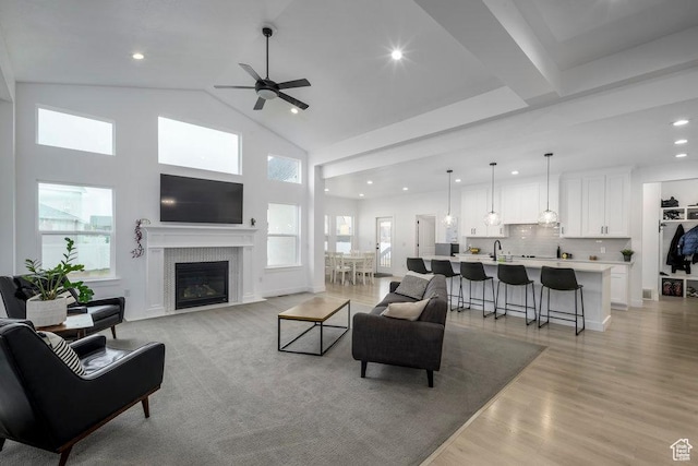 living room with recessed lighting, light wood-style floors, a glass covered fireplace, high vaulted ceiling, and a ceiling fan